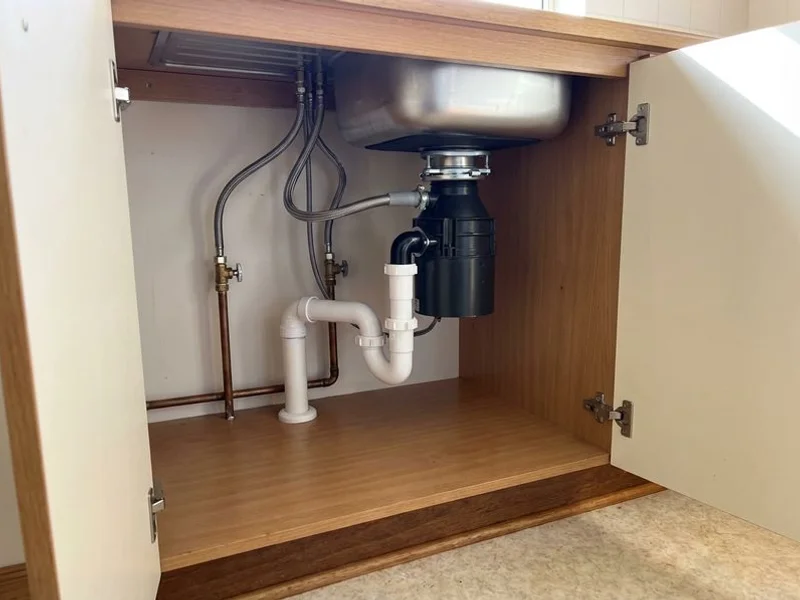 Under-sink plumbing with new waste trap and garbage disposal unit installed
